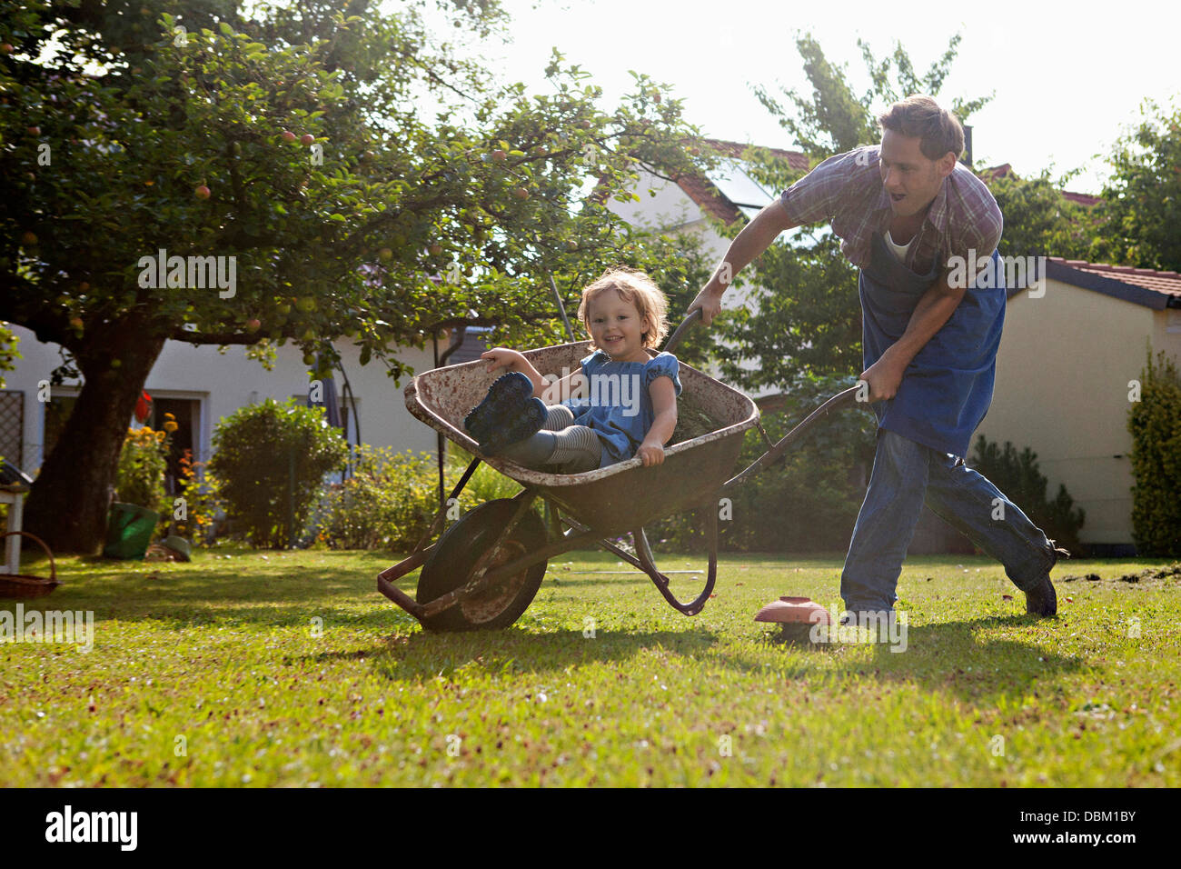 Father pushing wheelbarrow with daughter in the garden, Munich, Bavaria, Germany Stock Photo