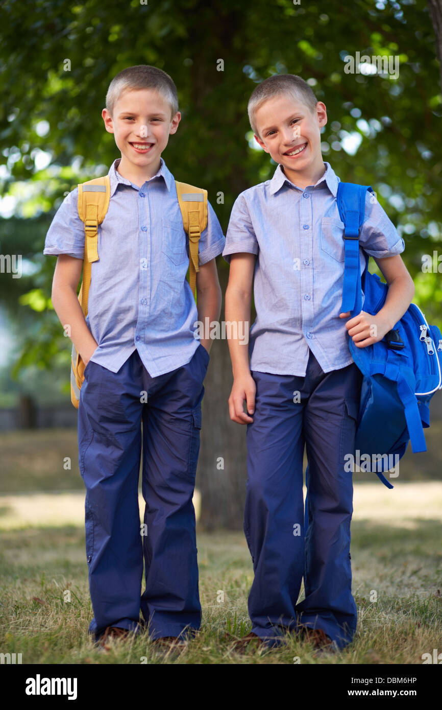 Image of cute twin boys with backpacks standing in summer park Stock Photo