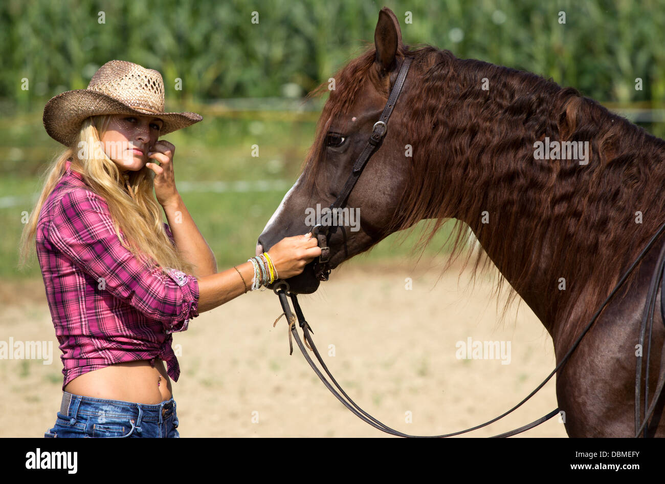 Beautiful blond woman holding brown horse. Stock Photo