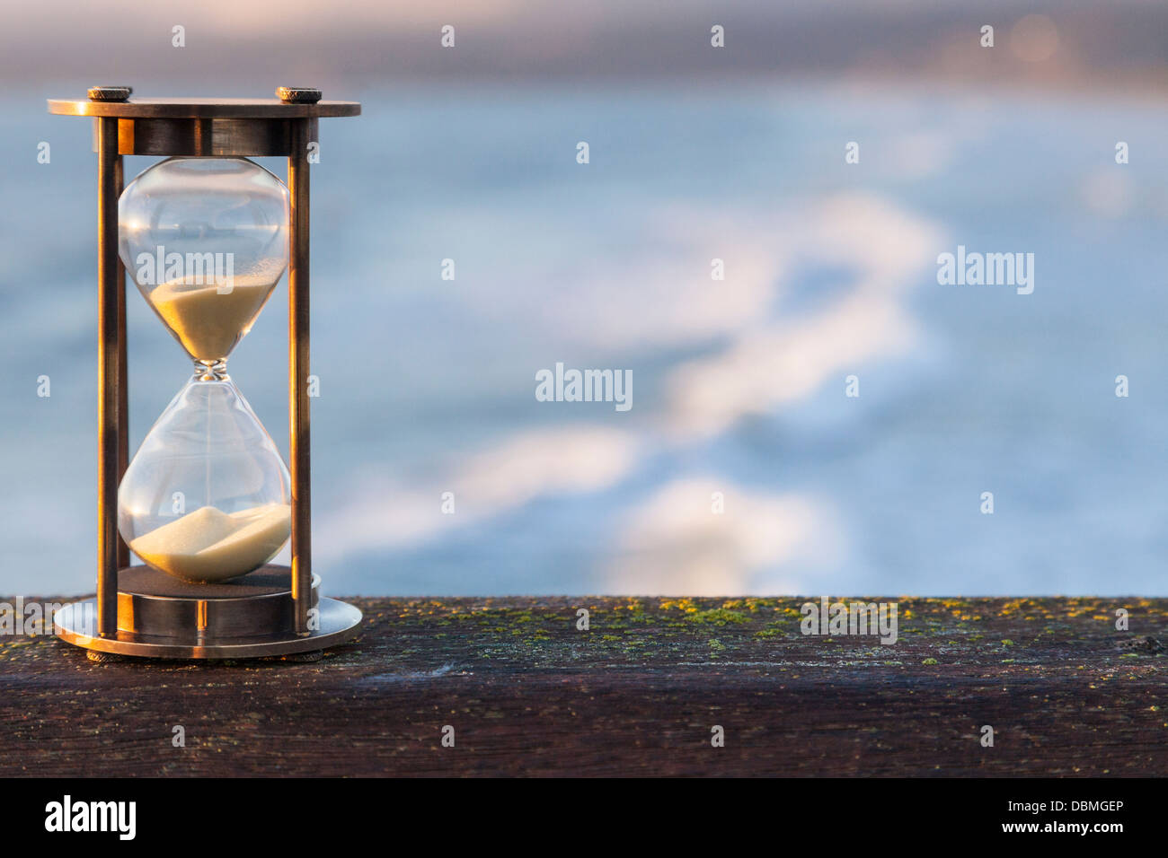 Hourglass Outdoors - sunlit hourglass or sand timer with a background of flowing water. Stock Photo