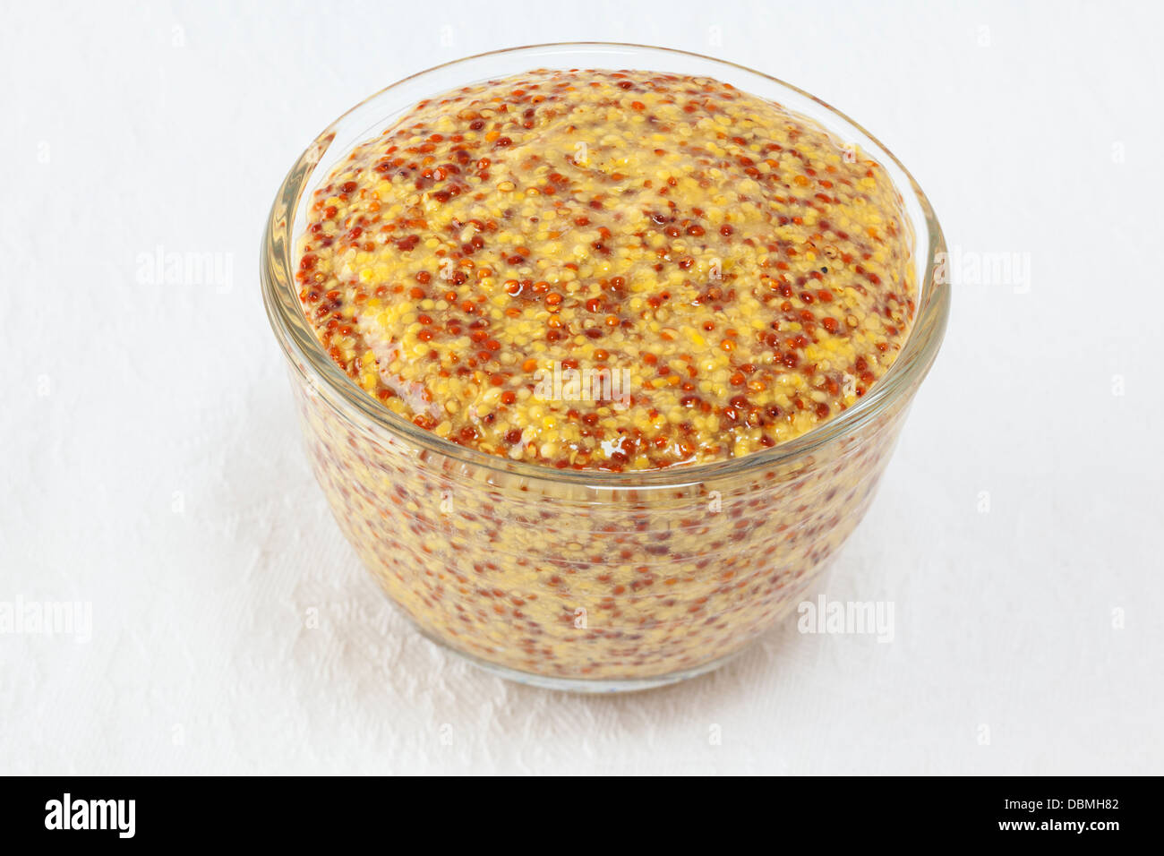 Wholegrain mustard in a small glass dish on a white textured cloth background. Stock Photo