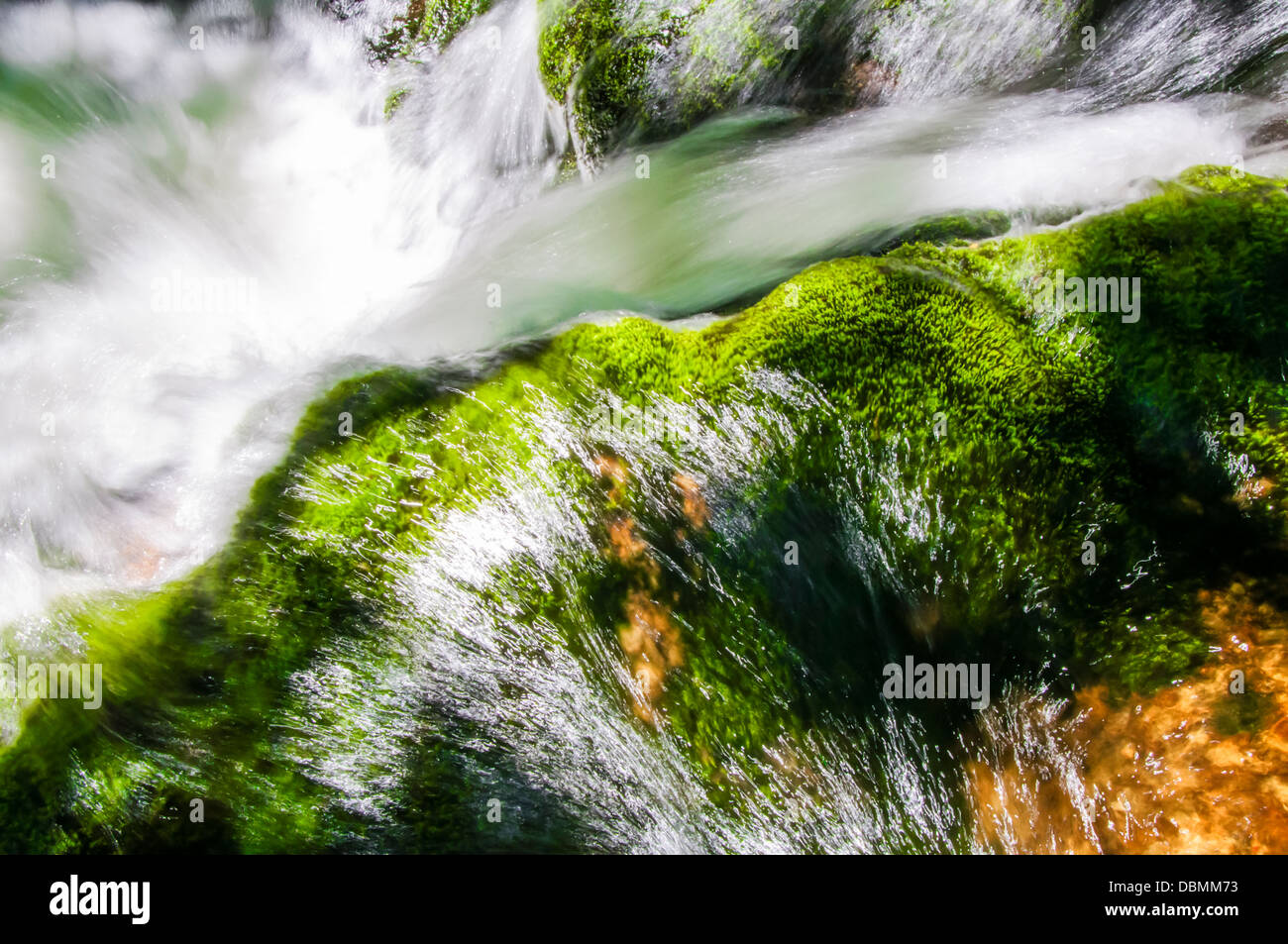 Crystal clear water flowing over green mossy rocks Stock Photo