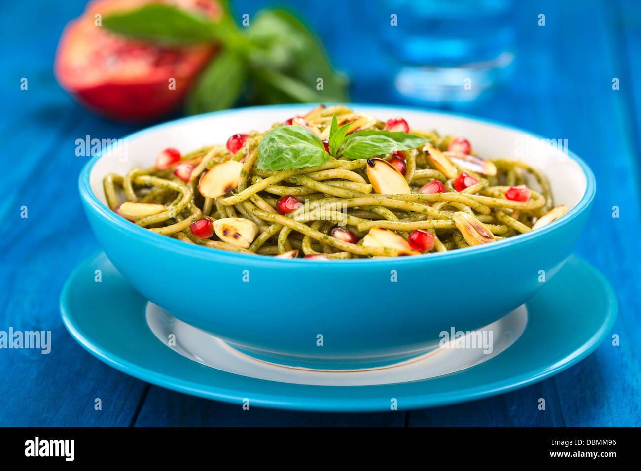 Spaghetti with pesto, pomegranate and roasted almond halves garnished with a basil leaf Stock Photo