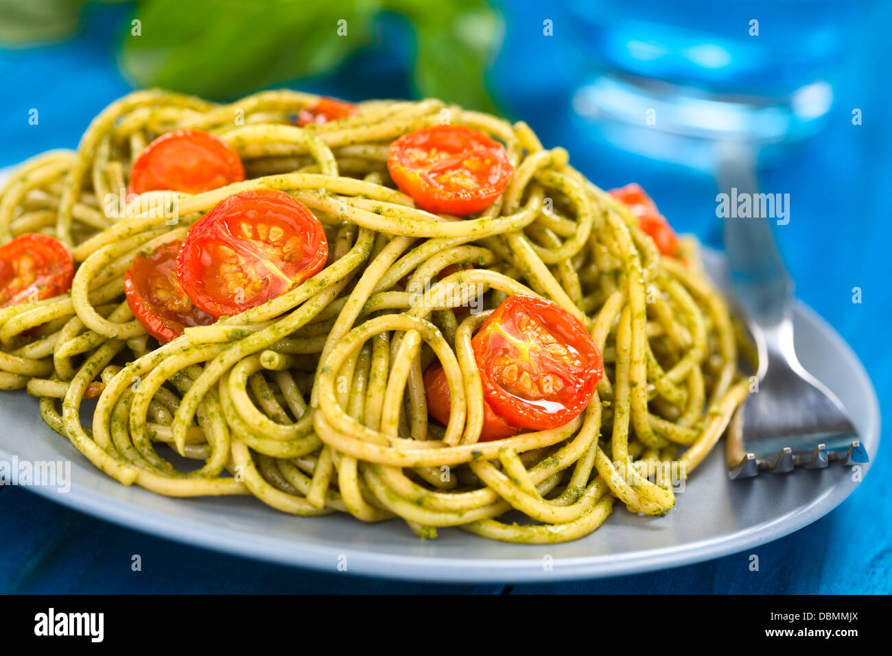 Spaghetti with pesto and baked cherry tomato halves served on a blue plate Stock Photo