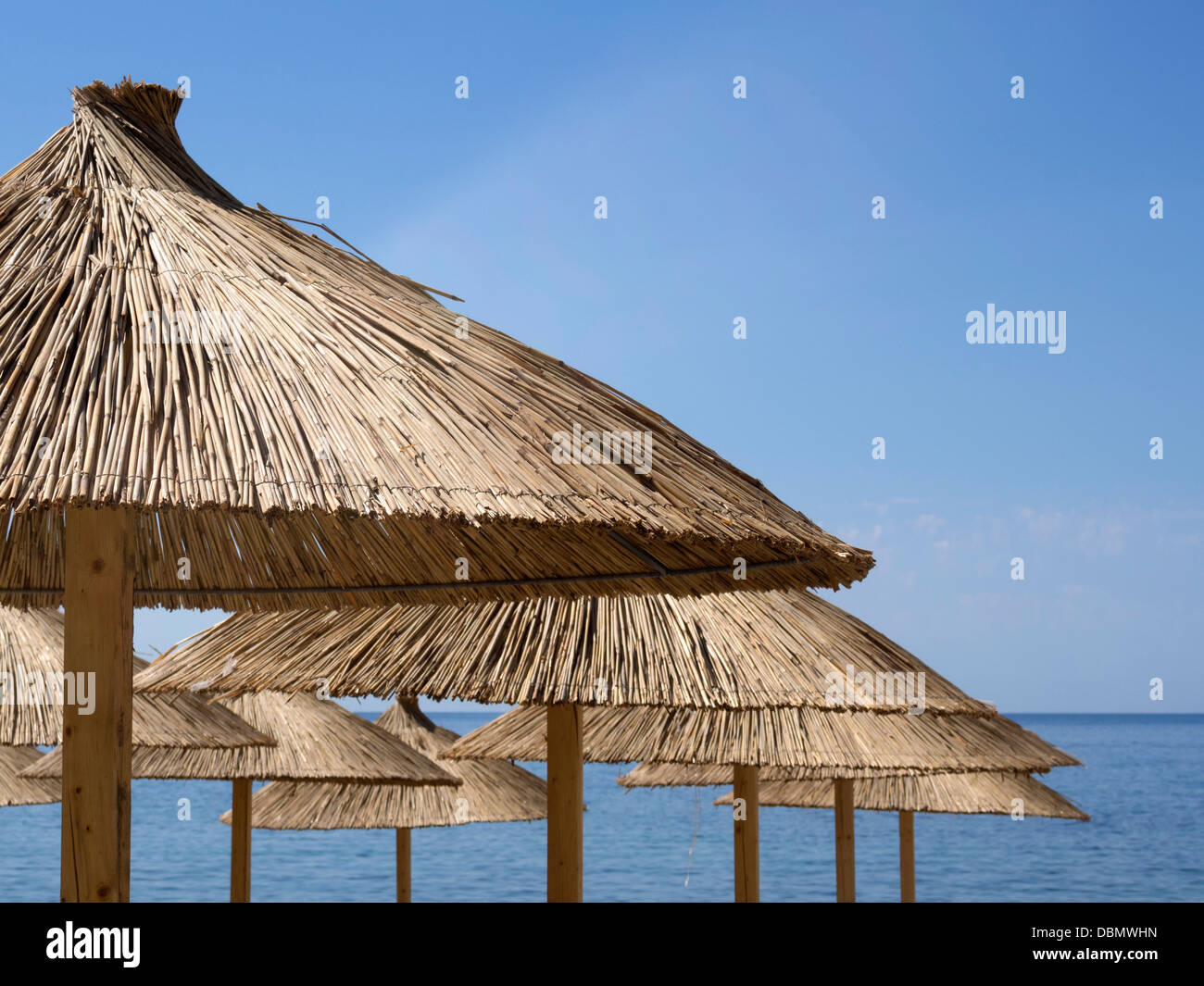 many straw sunshade parasols over blue sky and sea background with focus on front parasol Stock Photo