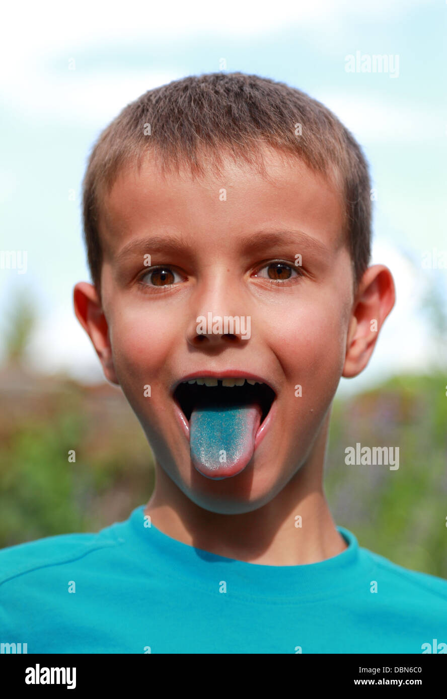 Face of a kid showing his tongue. His tongue is all blue. Focused on the face. 1 white kid of 7 years old. Stock Photo