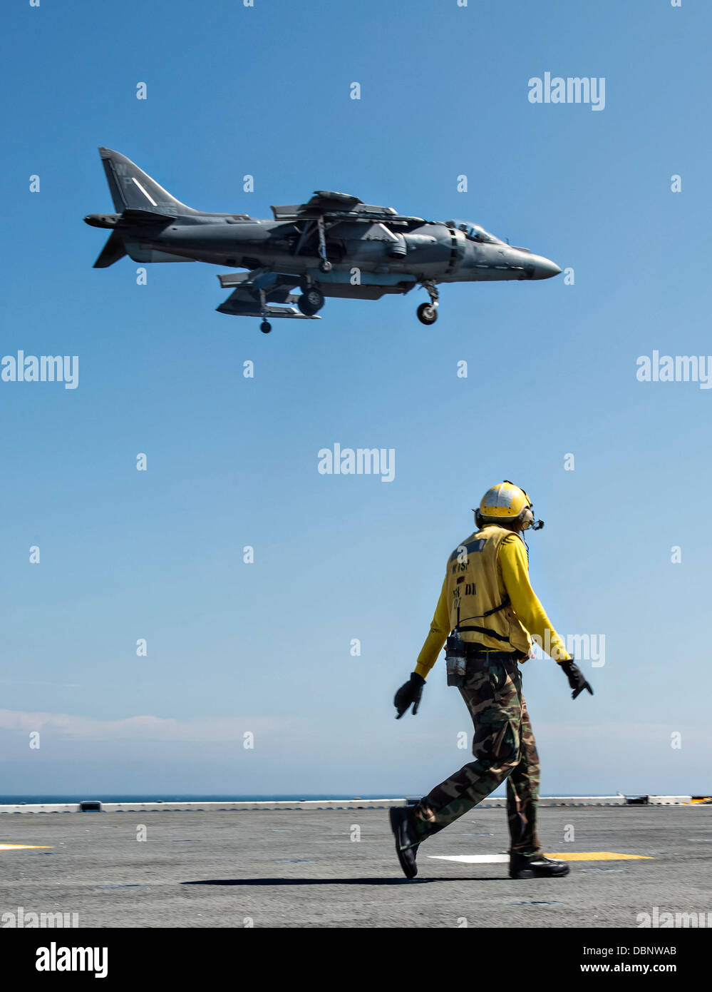 A US Navy Aviation Boatswain Mate watches a AV-8B II Harrier fighter jet land on the flight deck of the amphibious assault ship USS Wasp July 23, 2013 operating in the Atlantic Ocean. Stock Photo