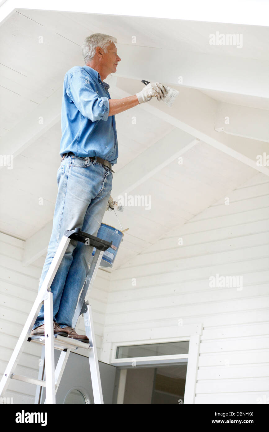 Senior man standing on ladder and painting wall Stock Photo - Alamy
