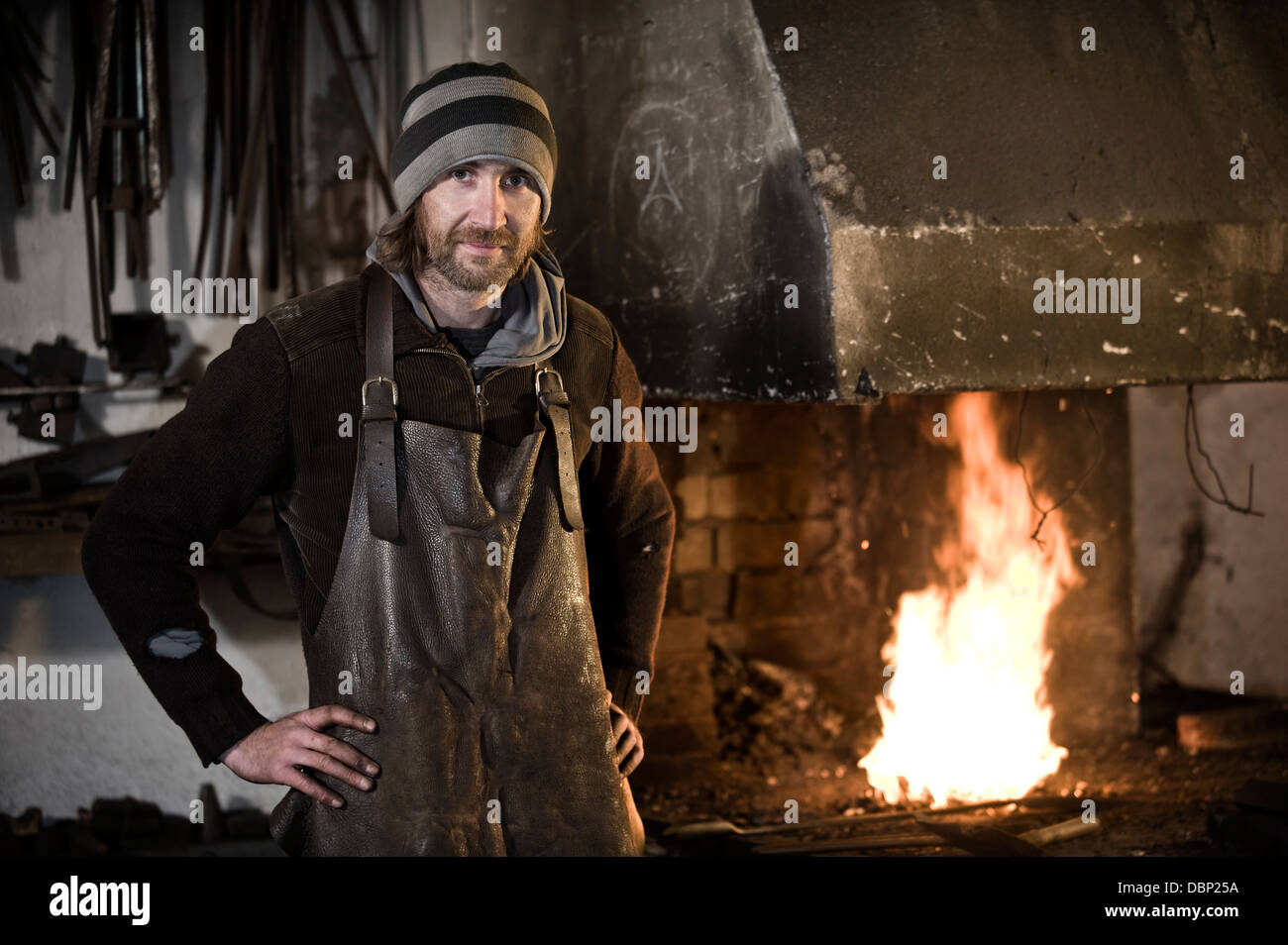 Blacksmith standing in workshop, forge in background, Landshut, Bavaria, Germany Stock Photo