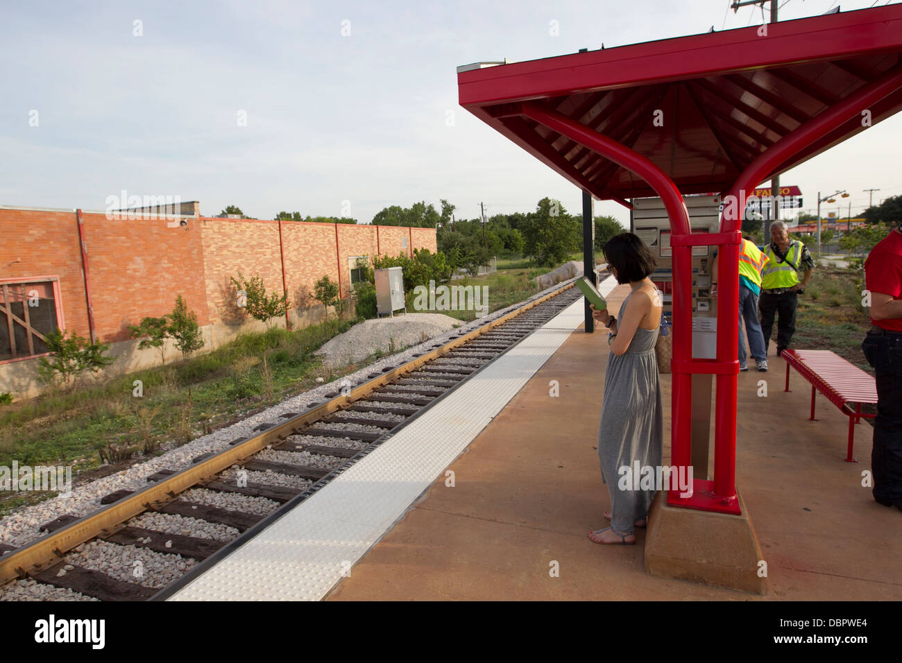 Woman reads on her ebook reader Kindle as she waits for a public transportation metro rail train on her morning commute Stock Photo