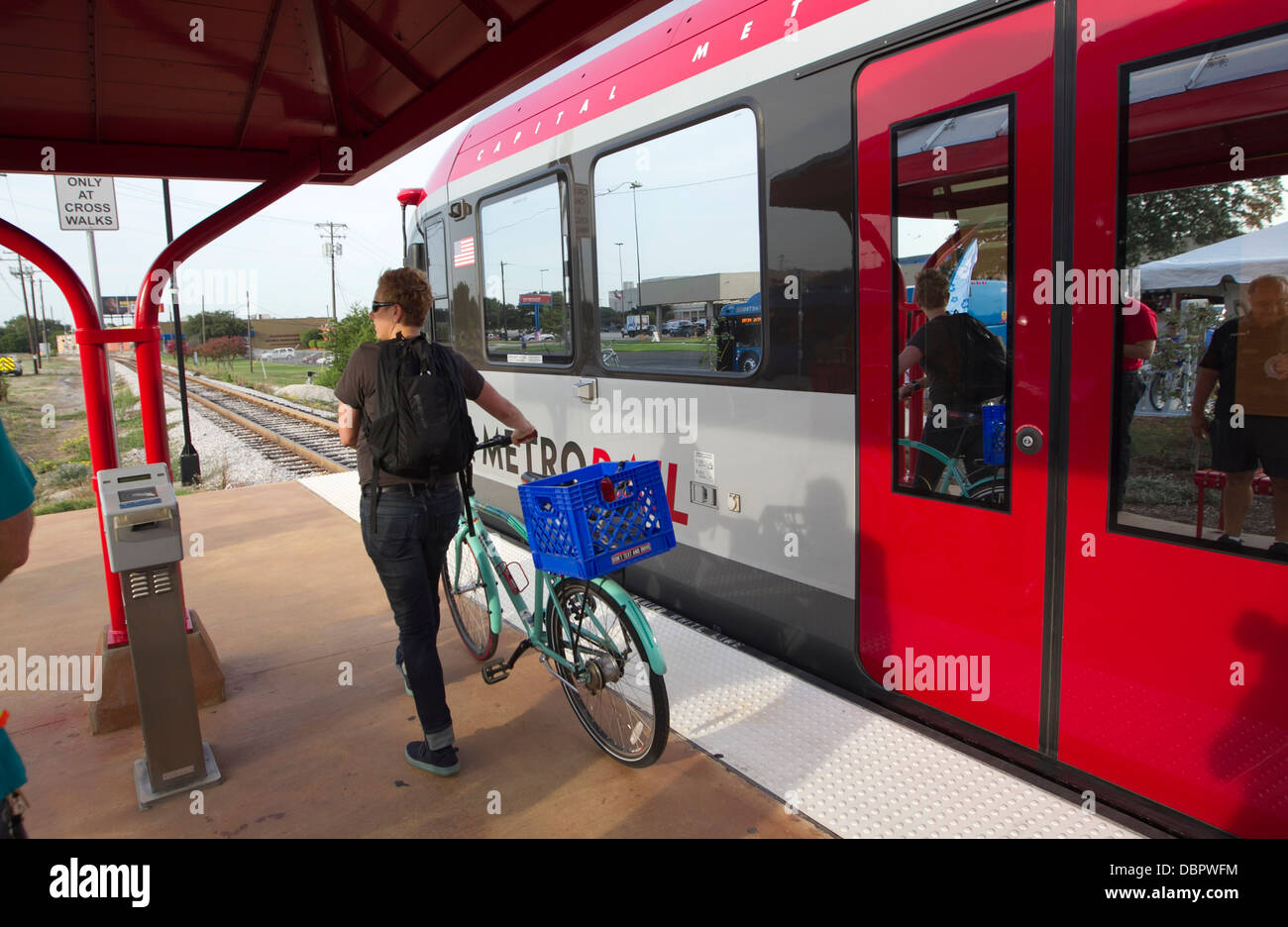 Female commuter exits a metro-rail train with her bicycle at a public transportation stop in Austin, Texas Stock Photo