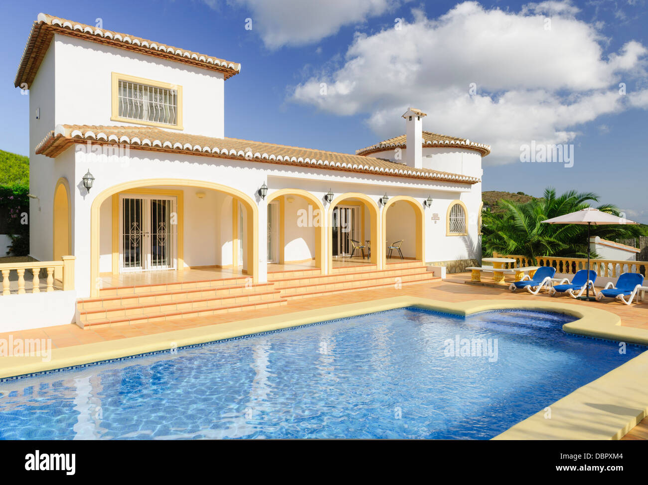 A holiday villa, complete with pool, basks in the Spanish sunshine whilst a series of fluffy white clouds pass by overhead. Stock Photo