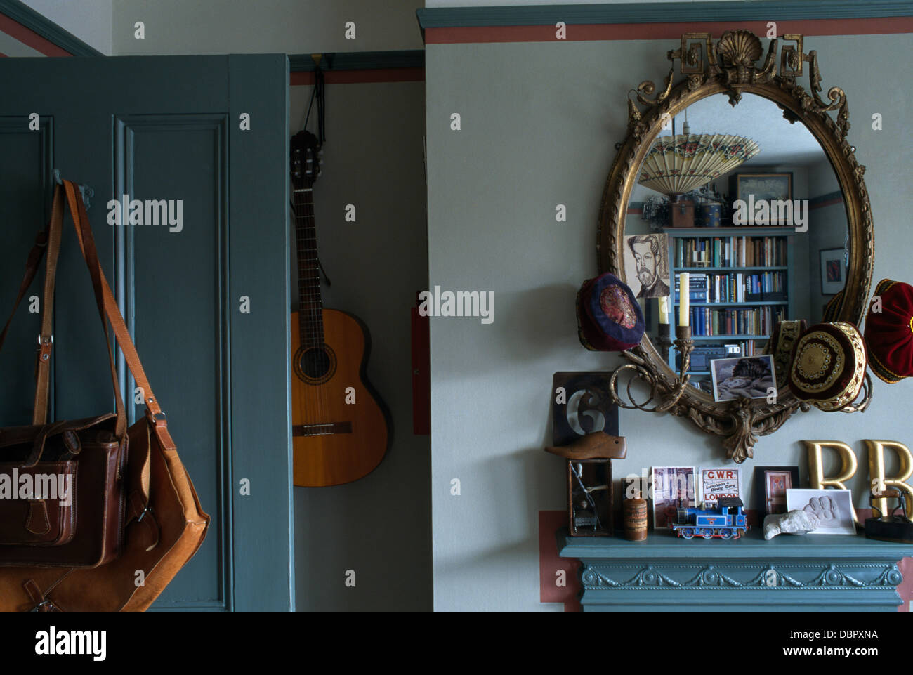 Antique girandole mirror above fireplace in small townhouse bedroom with guitar and old leather satchels hanging on pegs Stock Photo