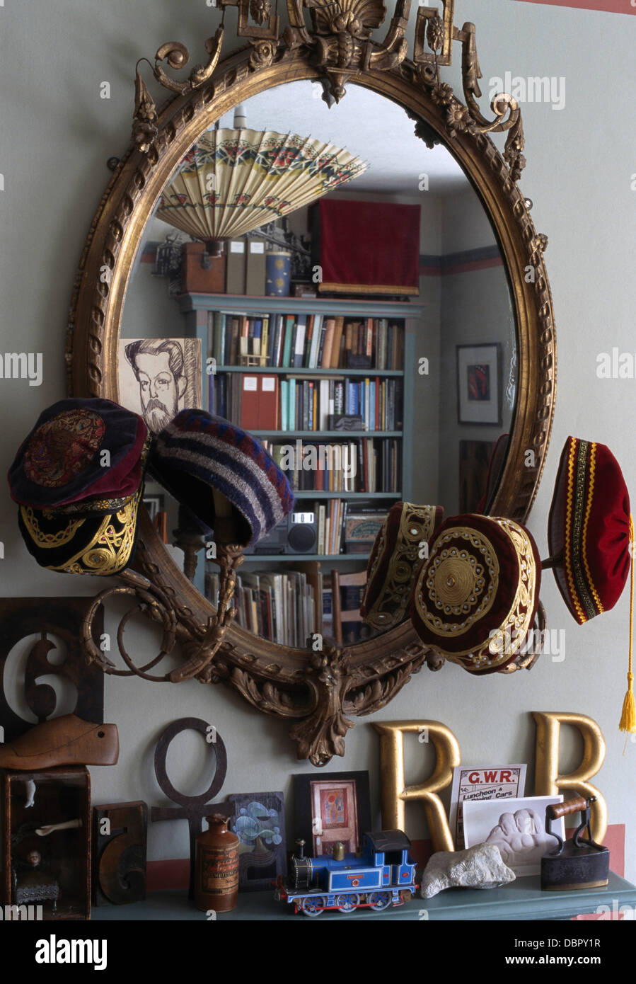 Close-up of antique girandole mirror with a collection of Muslim Taqiyah caps  above shelf with painted wooden letters Stock Photo