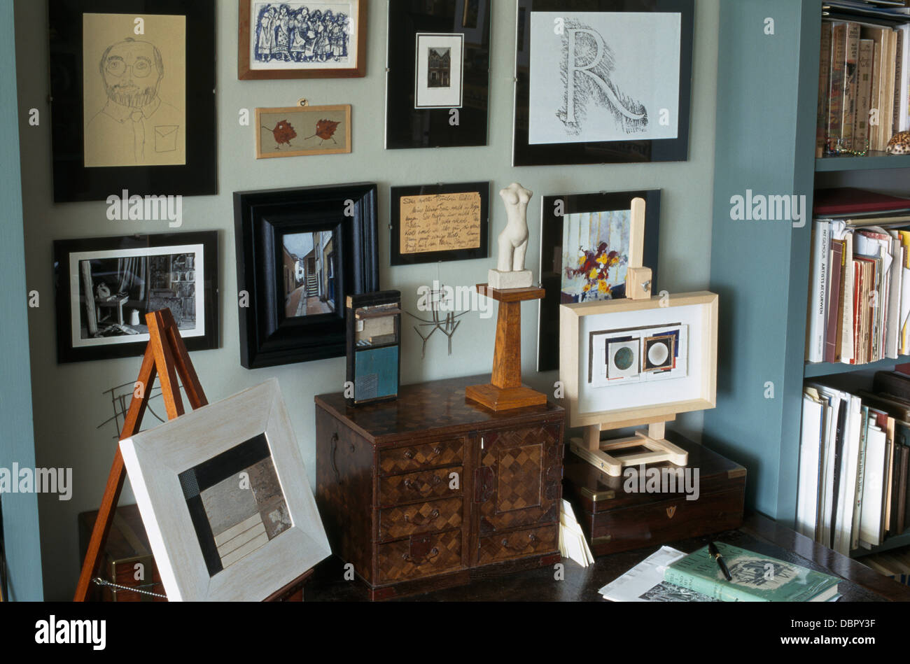 Collection of pictures on wall above desk with antique box and small painting on easel Stock Photo