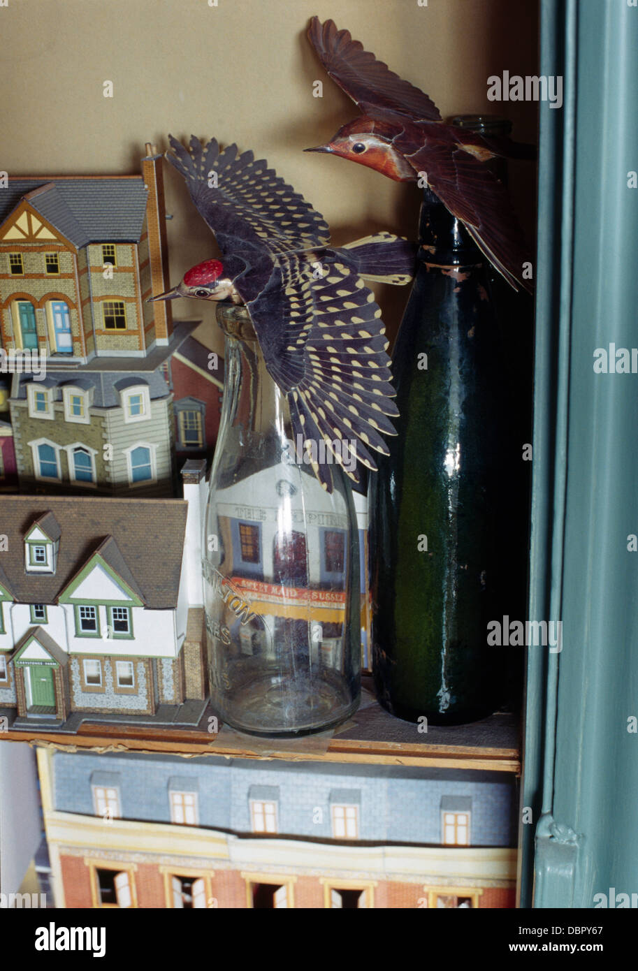 Close-up of wooden birds on old milk bottles beside small dolls houses Stock Photo