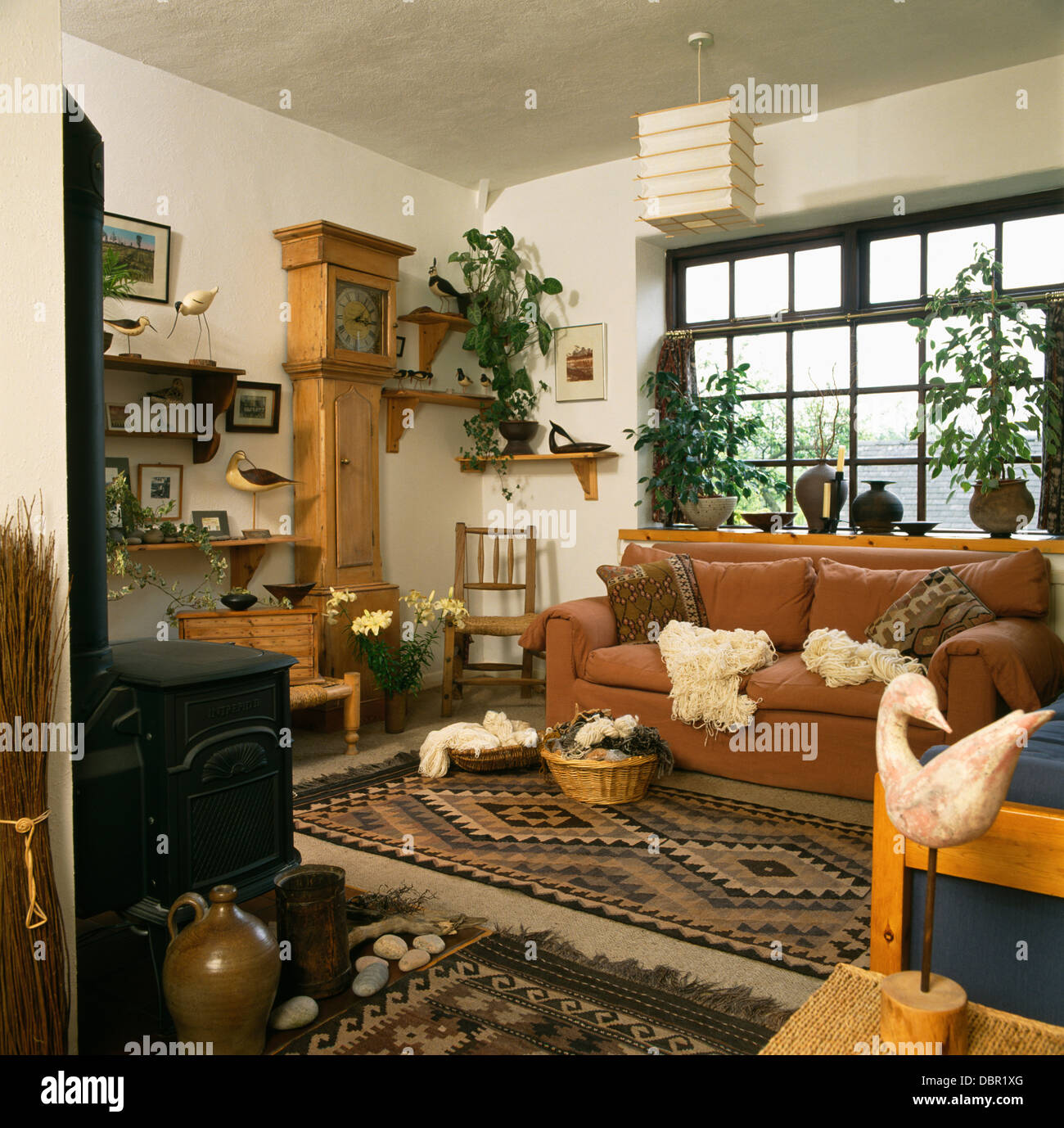 Baskets of wool and patterned rug in economy-style living room with pine long case clock and wood-burning stove Stock Photo