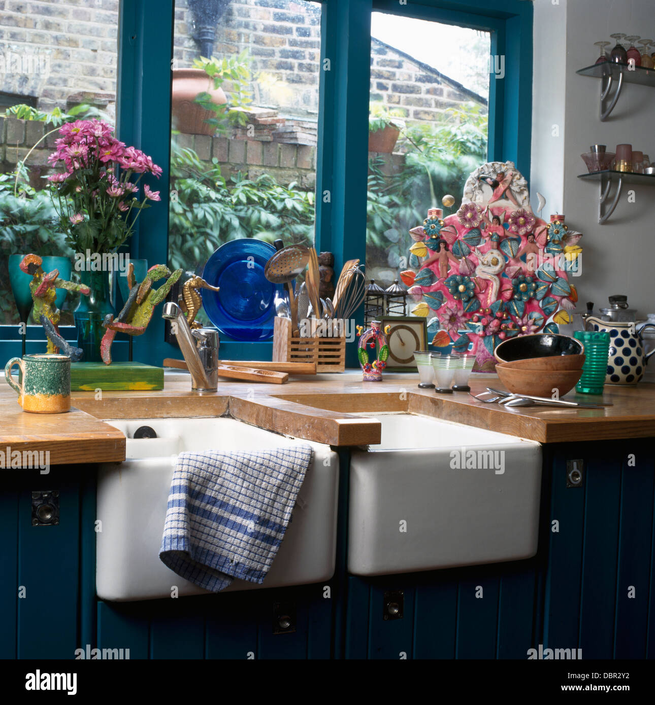 Double Belfast sinks below turquoise window in cottage kitchen with