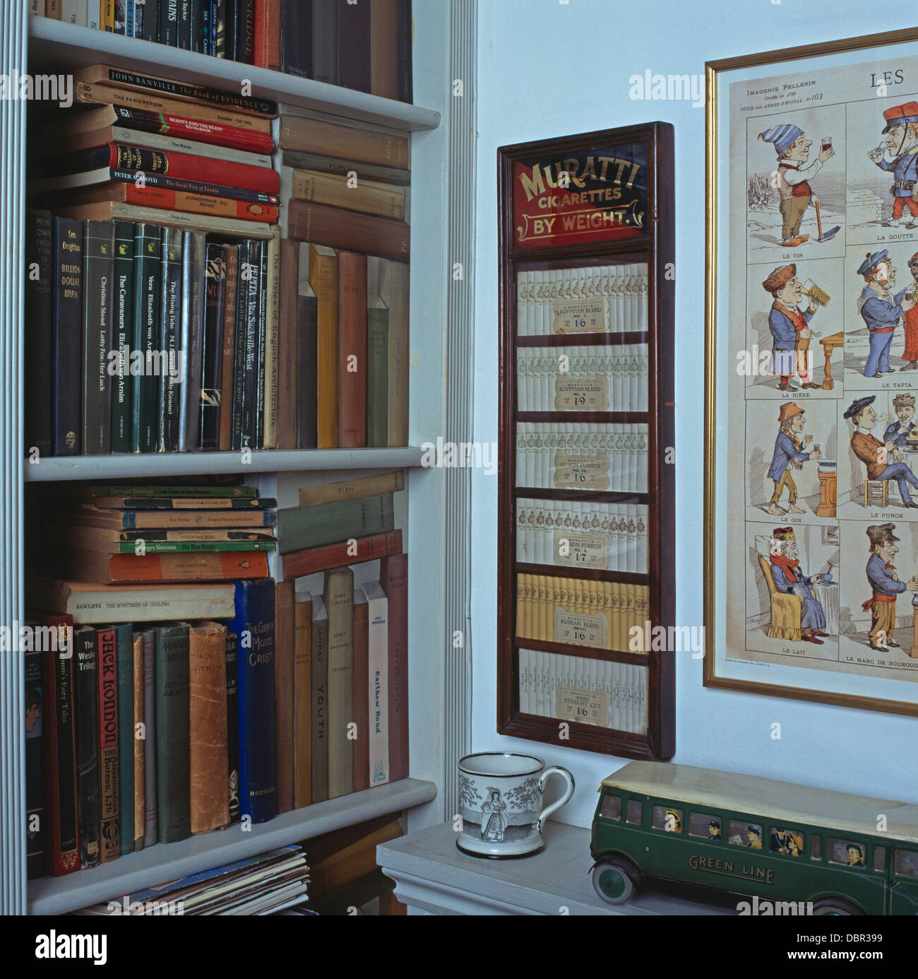 Books on shelves with trompe-l'oeil book panels beside framed Muratti cigarettes in small hall Stock Photo