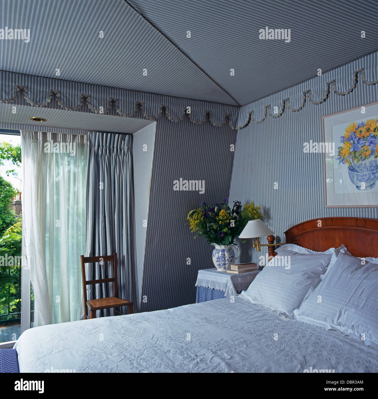 Blue+white striped fabric on walls and ceiling with matching cornice in bedroom with white voile and striped curtains Stock Photo