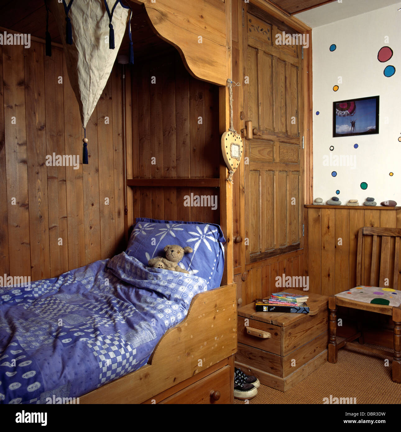 Blue+white duvet and pillow on wooden bed enclosed with wood paneling in child's bedroom with wooden box step to door Stock Photo