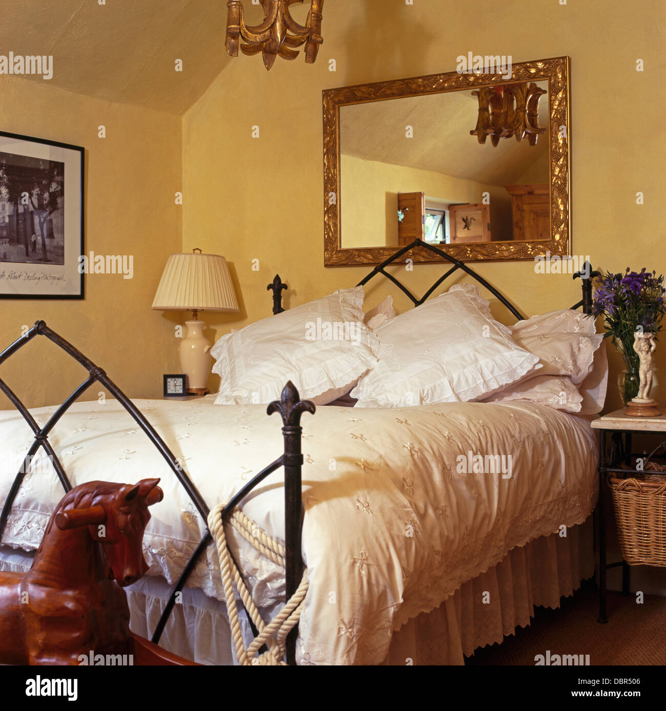 Gilt mirror above Gothicstyle wroughtiron bed with white duvet and