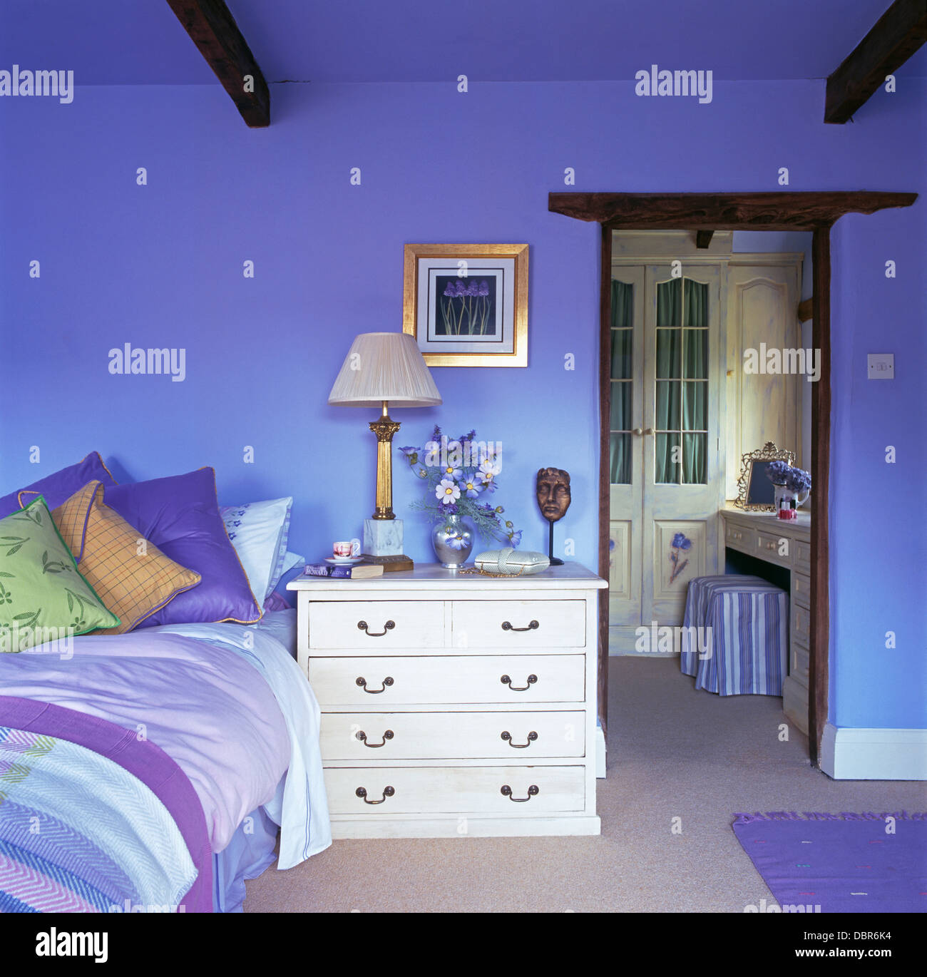 White Chest Of Drawers Beside Bed Piled With Colorful Cushions In