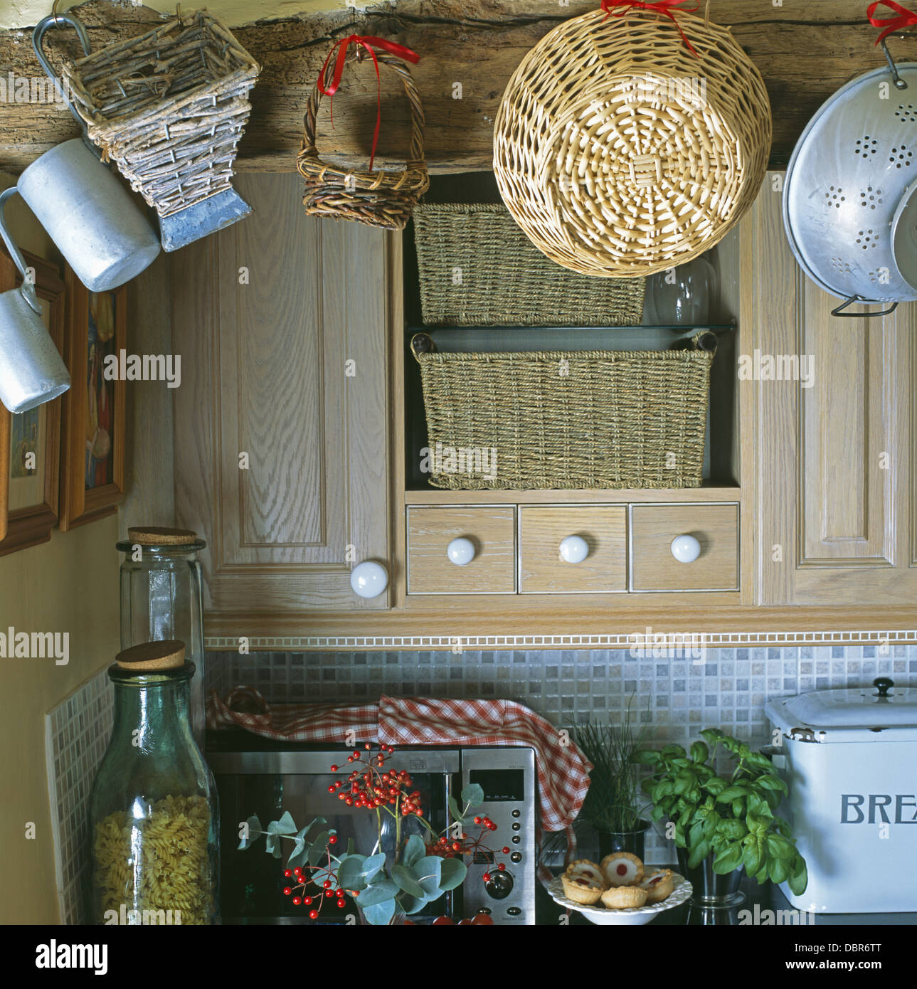 Closeup of baskets on beam above kitchen wall cupboard with storage baskets on shelves Stock