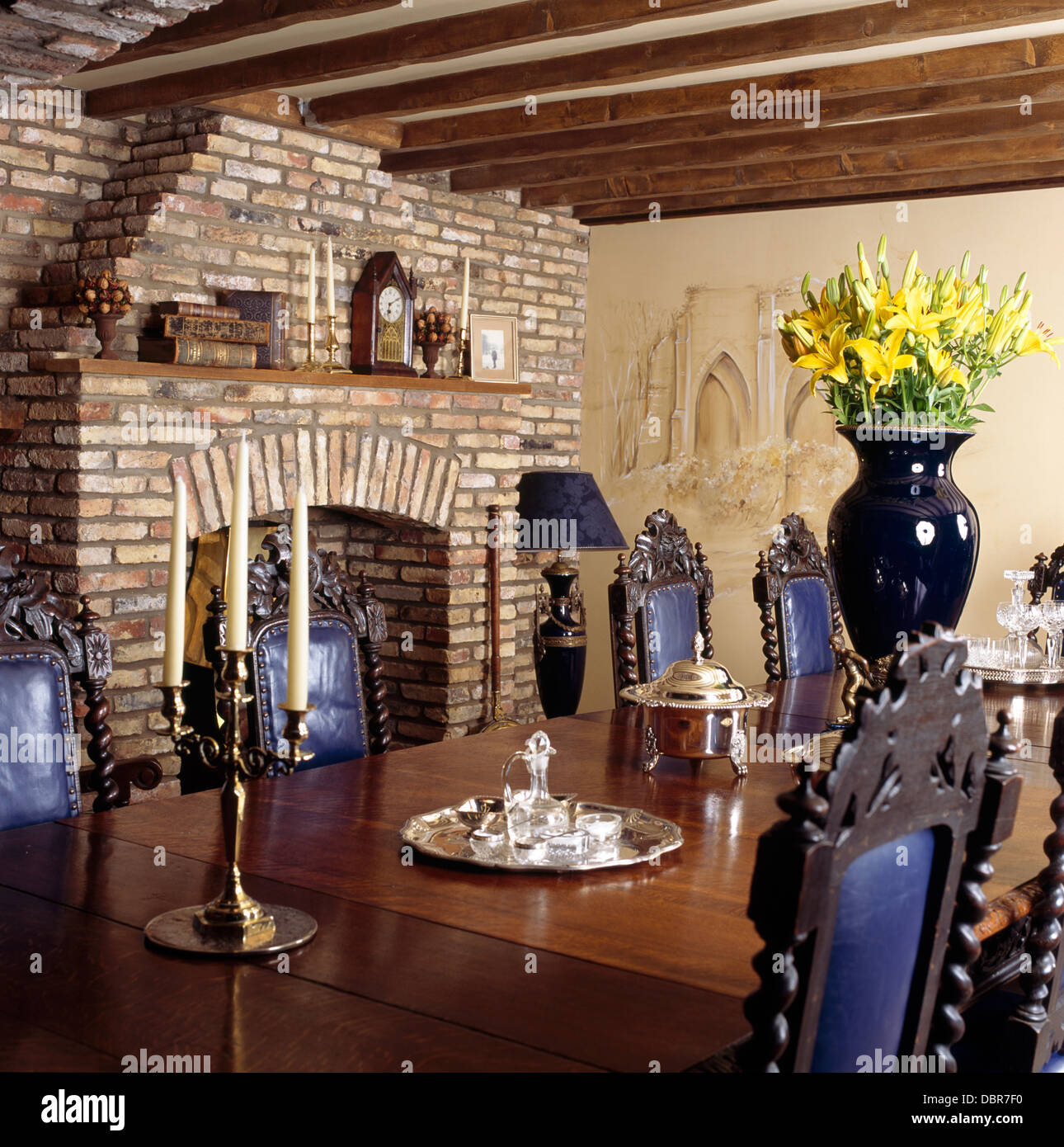 Vase of yellow lilies on table with Jacobean-style chairs with blue leather backs in beamed country dining room Stock Photo