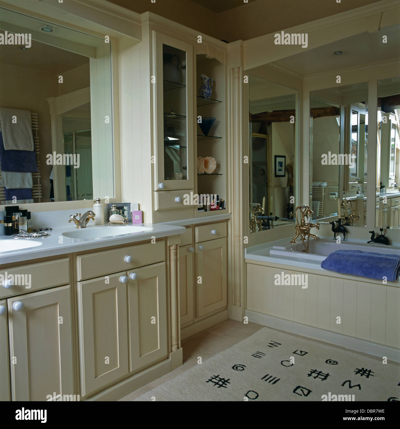 Mirrored wall above alcove bath in country bathroom with black+white oriental-script patterned rug Stock Photo