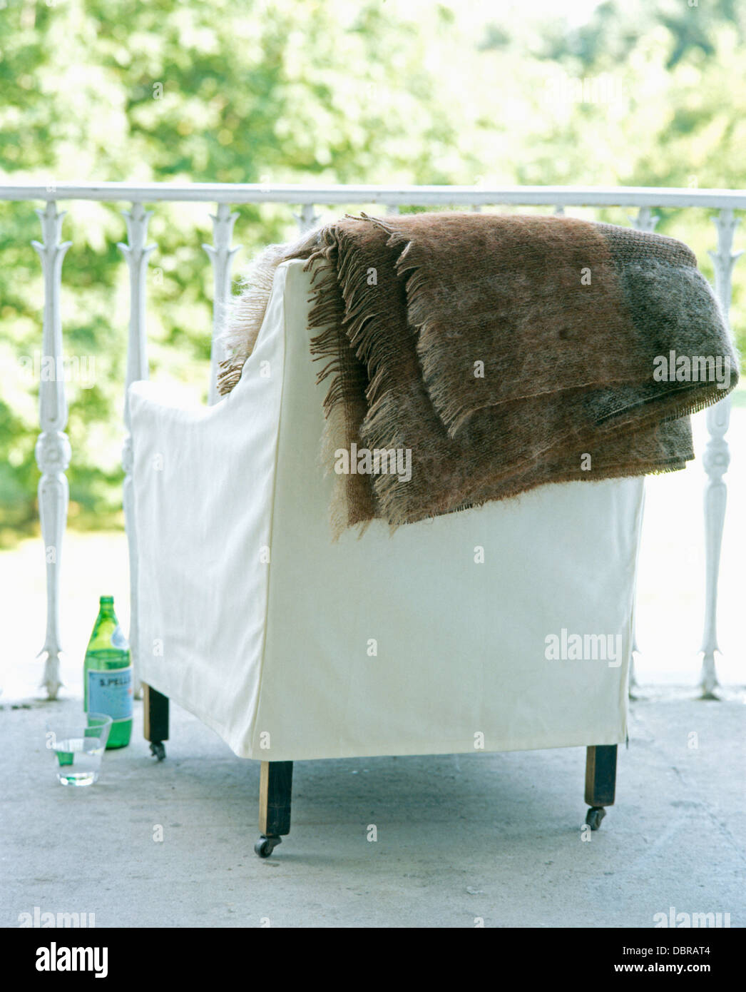 Close-up of brown+gray mohair rug on the back of chair with white linen loose cover on balcony Stock Photo