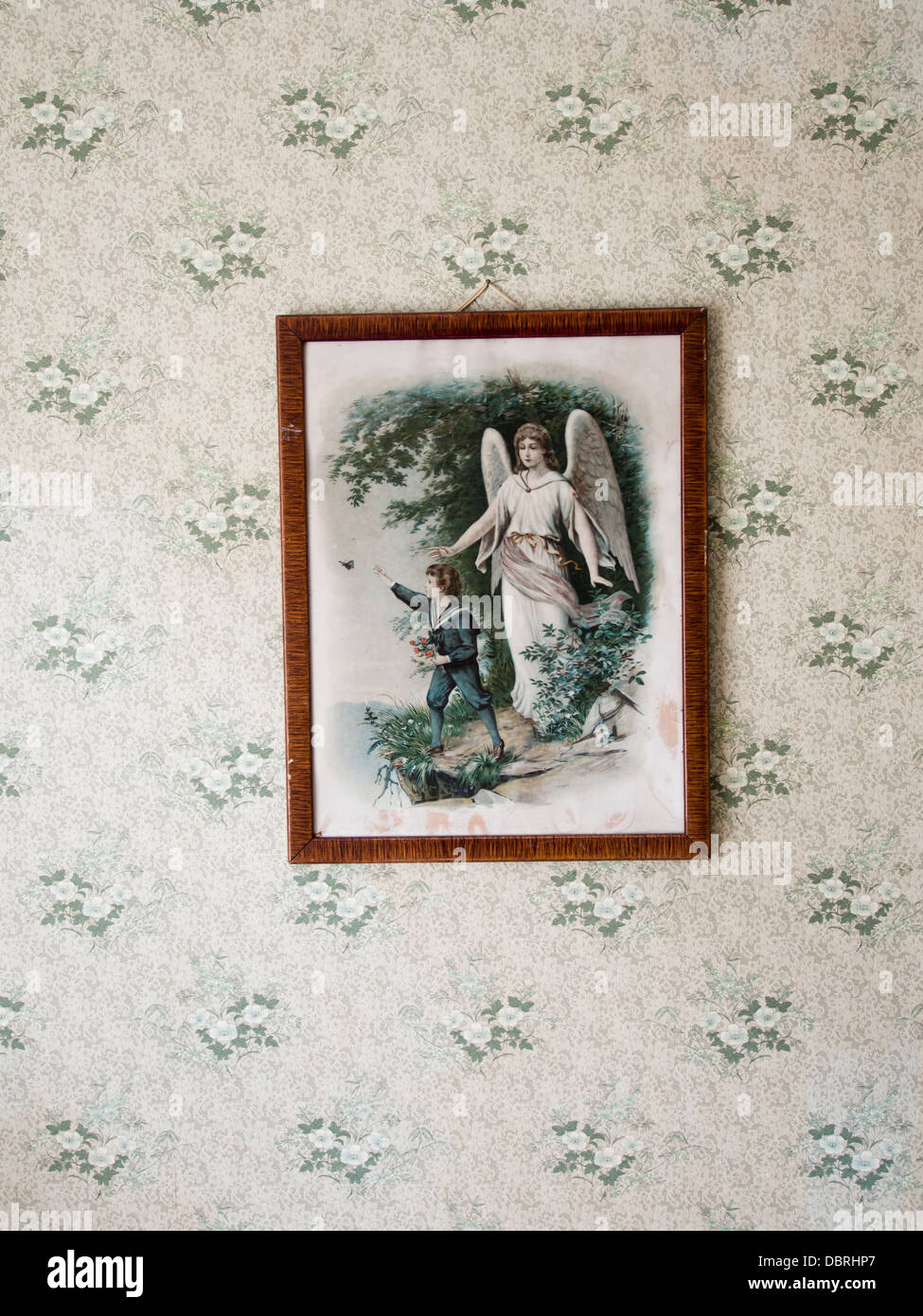 Religious print, brown frame, flower patterned wallpaper, angel protecting young boy on edge of cliff,  vintage decoration Stock Photo