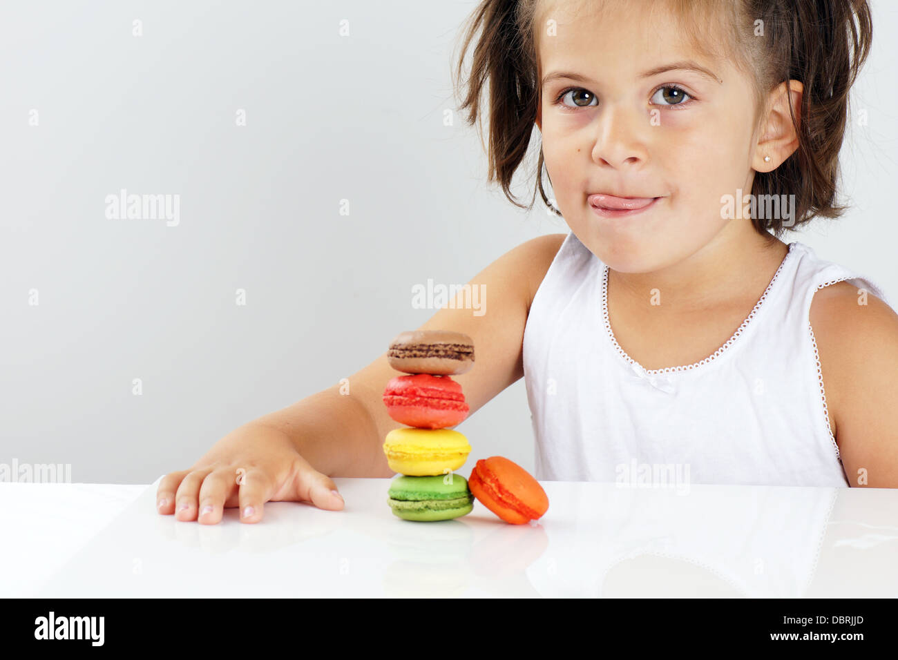 Cute little girl licking her lips in front of colorful stack of macaroons Stock Photo