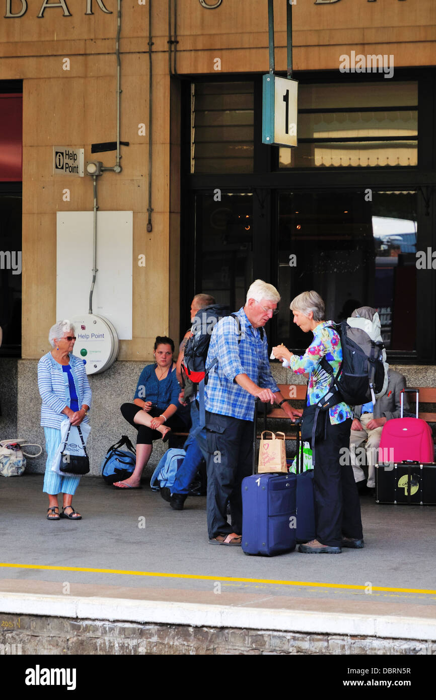 An elderly couple with luggage waiting on the platform for a train at