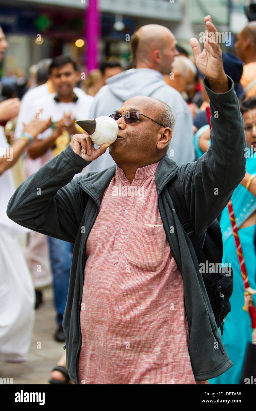 Leicester, UK, 4th August 2013.  A Hare Krishna follower blows a conch shell during the Rathayatra street festival in Leicester's City Centre.   Three 40ft chariots were hand pulled through the City, accompanied by dance and music.  Rathayatra is a 5,000 year old festival originating in Jagannatha Puri in India. Credit:  Graham Wilson/Alamy Live News Stock Photo