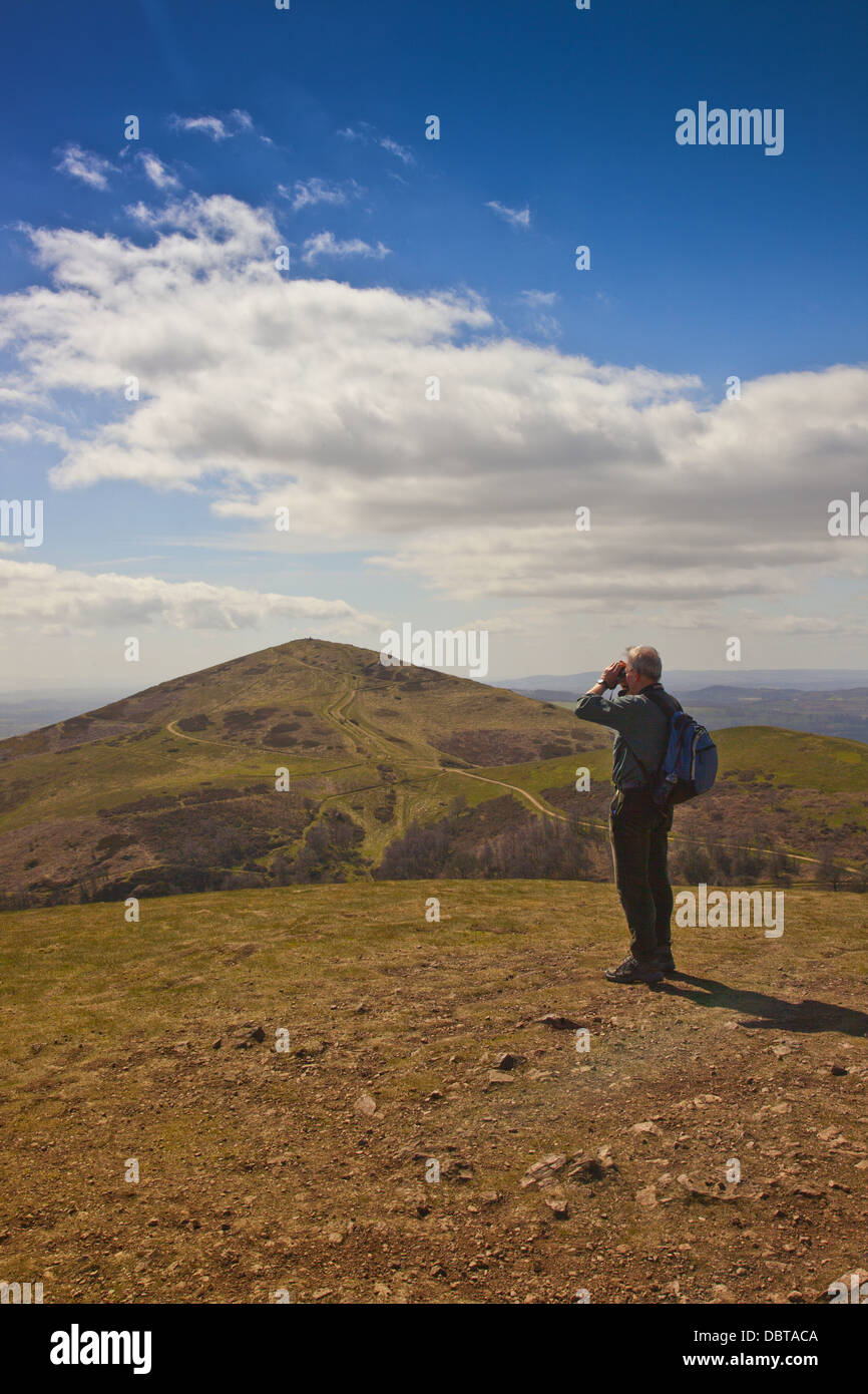 A walker with binoculars on the summit of North Hill in the Malvern Hills, Worcestershire, England, UK Stock Photo