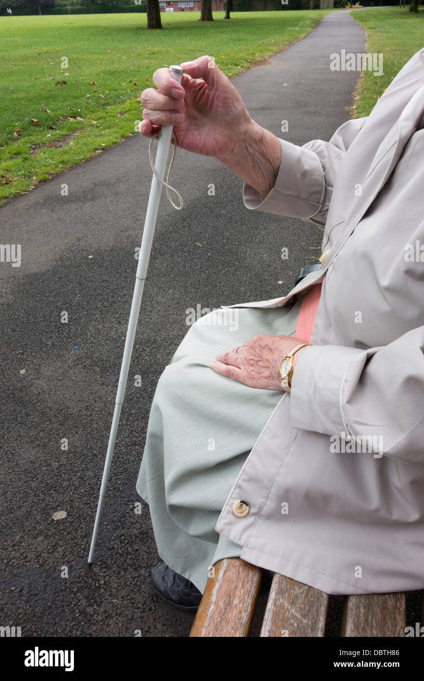 Ninety year old visually impaired lady with white stick sitting on bench in public park. England, UK Stock Photo