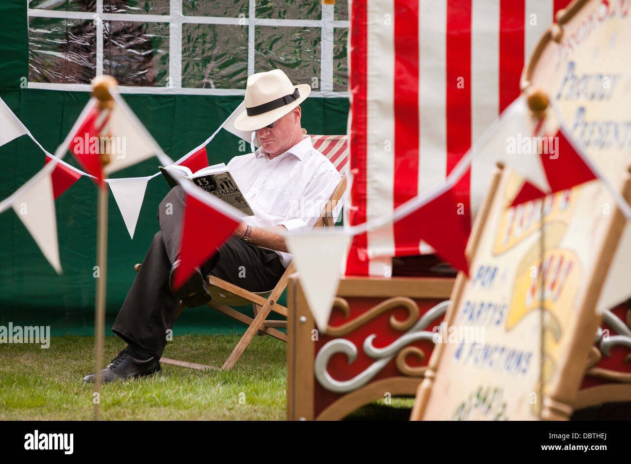 a man reads a book in the sun before perfroming a Punch and Judy show summer england english Stock Photo