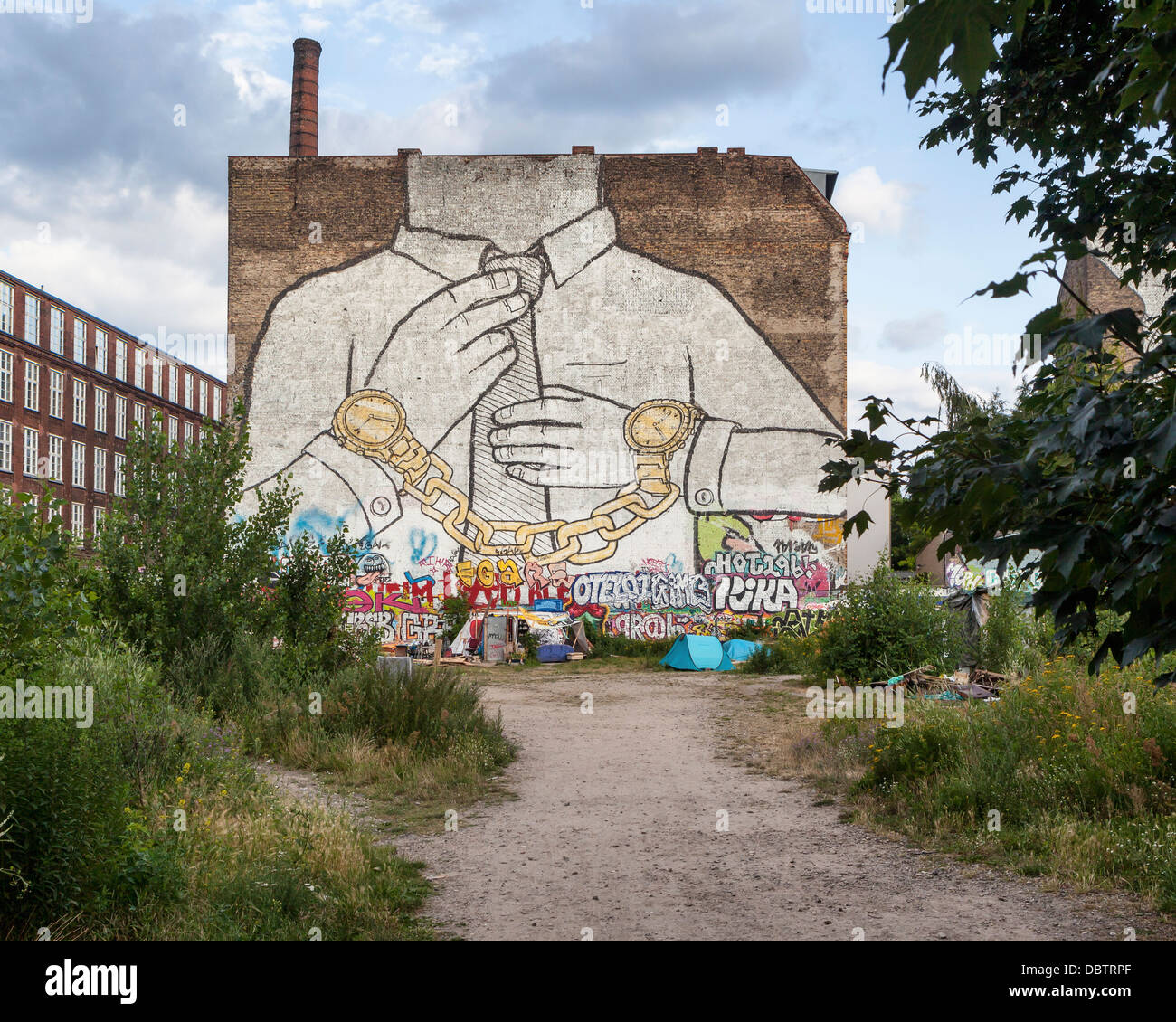 Giant Mural by street artist, Blu. A hand-cuffed man wearing two Rolex watches which are connected by a gold chain - Kreuzberg Stock Photo