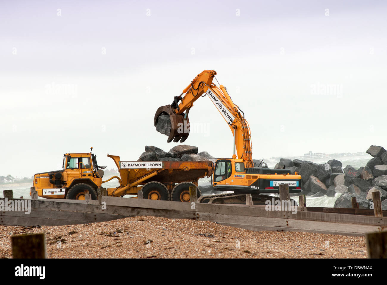 JCB loading a truck with large rocks to build up coastal defence on Hayling Island Stock Photo