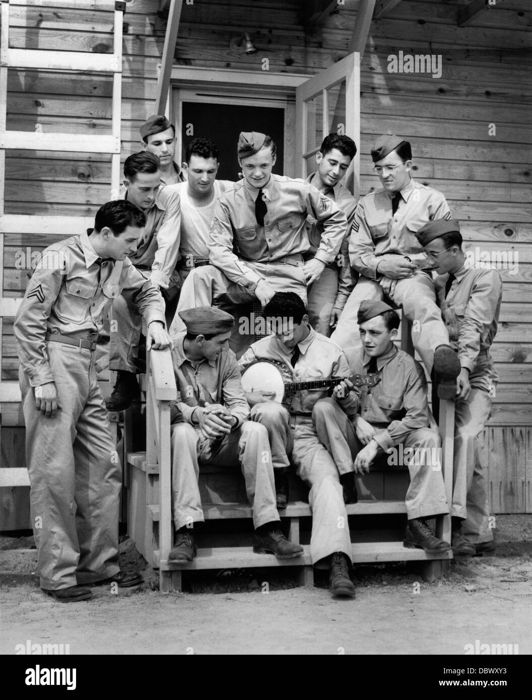 1940s GROUP OF SOLDIER SITTING ON STEPS OF BARRACKS LISTENING TO MAN PLAYING BANJO Stock Photo