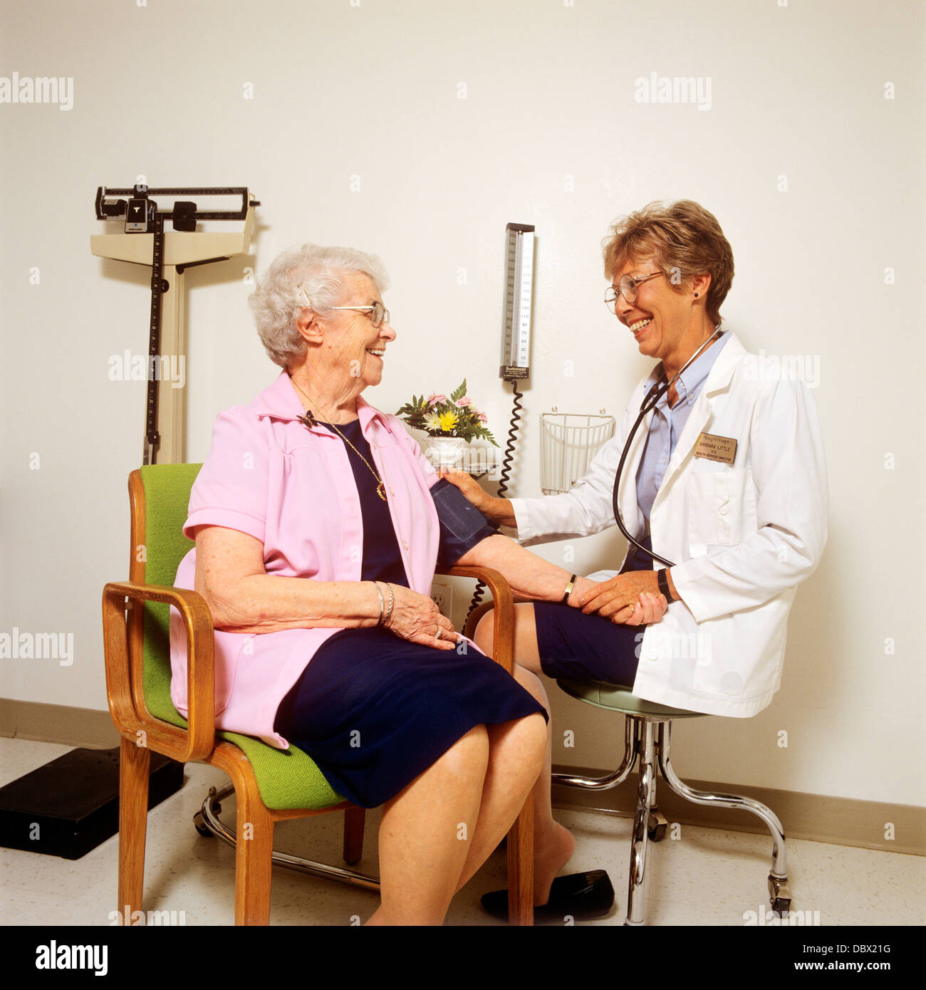 1990s WOMAN NURSE CHECKING BLOOD PRESSURE OF ELDERLY WOMAN PATIENT Stock Photo
