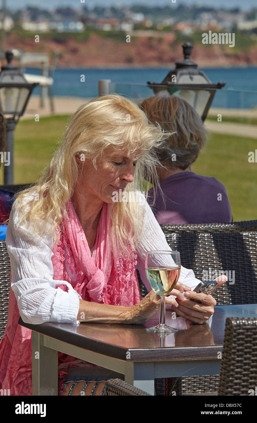 An attractive mature woman relaxing with a glass of wine at a restaurant's outdoor terrace. Stock Photo