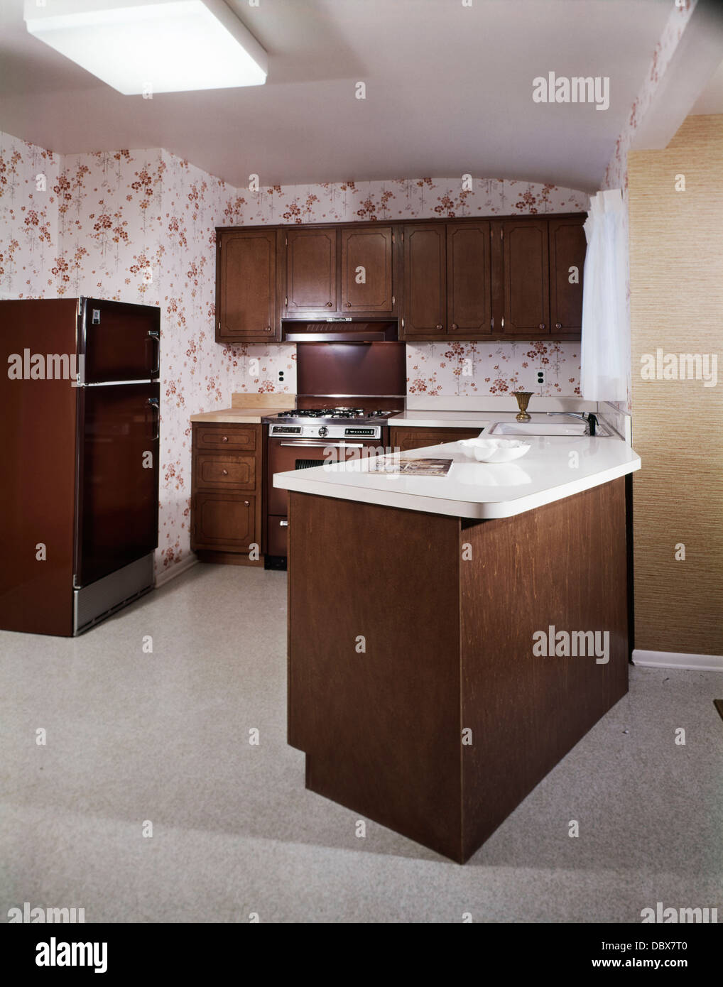 1970 1970s RETRO KITCHEN WITH DINING COUNTER ISLAND DARK WOODEN CABINETS AND APPLIANCES RUST AND WHITE WALLPAPER Stock Photo