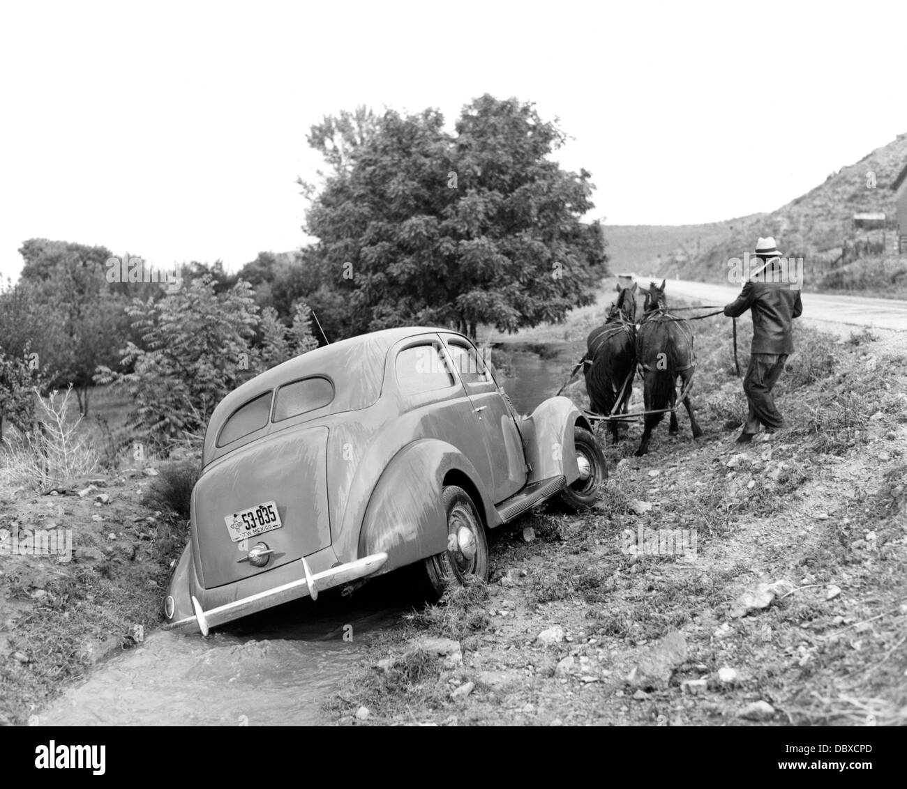 1930s 1937 FORD V-8 BEING PULLED OUT OF RURAL ROAD DITCH BY MAN WITH TEAM OF TWO HORSES Stock Photo