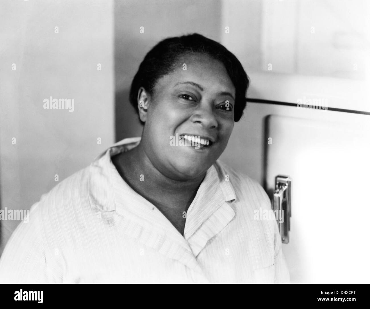 1930s 1940s PORTRAIT SMILING AFRICAN AMERICAN WOMAN DOMESTIC BY REFRIGERATOR IN KITCHEN LOOKING AT CAMERA Stock Photo