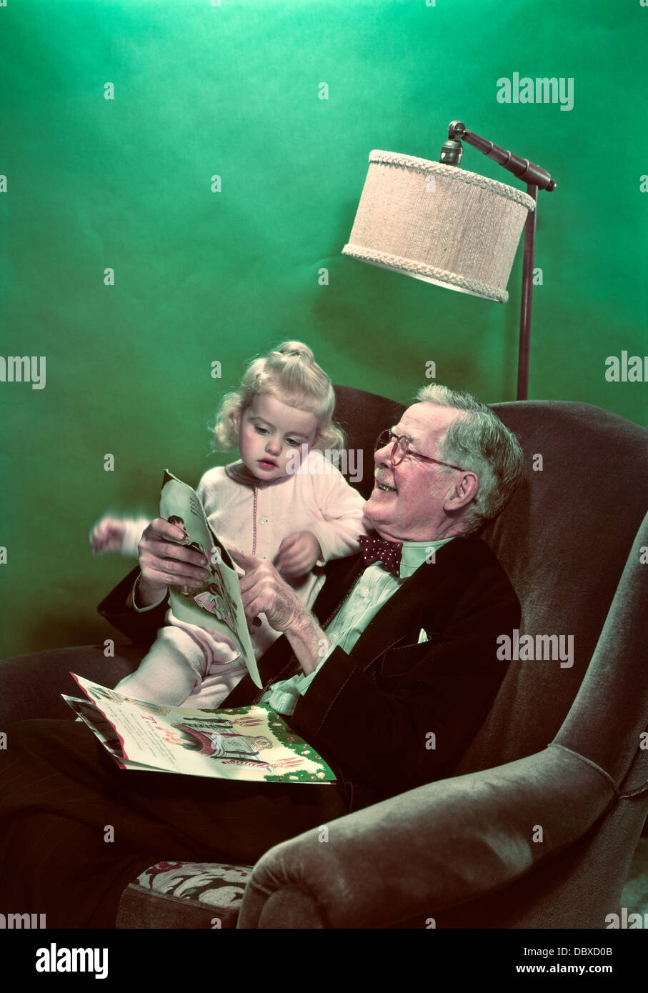 1940s 1950s GRANDDAUGHTER SITTING ON SMILING GRANDFATHER’S LAP READING PICTURE BOOKS Stock Photo