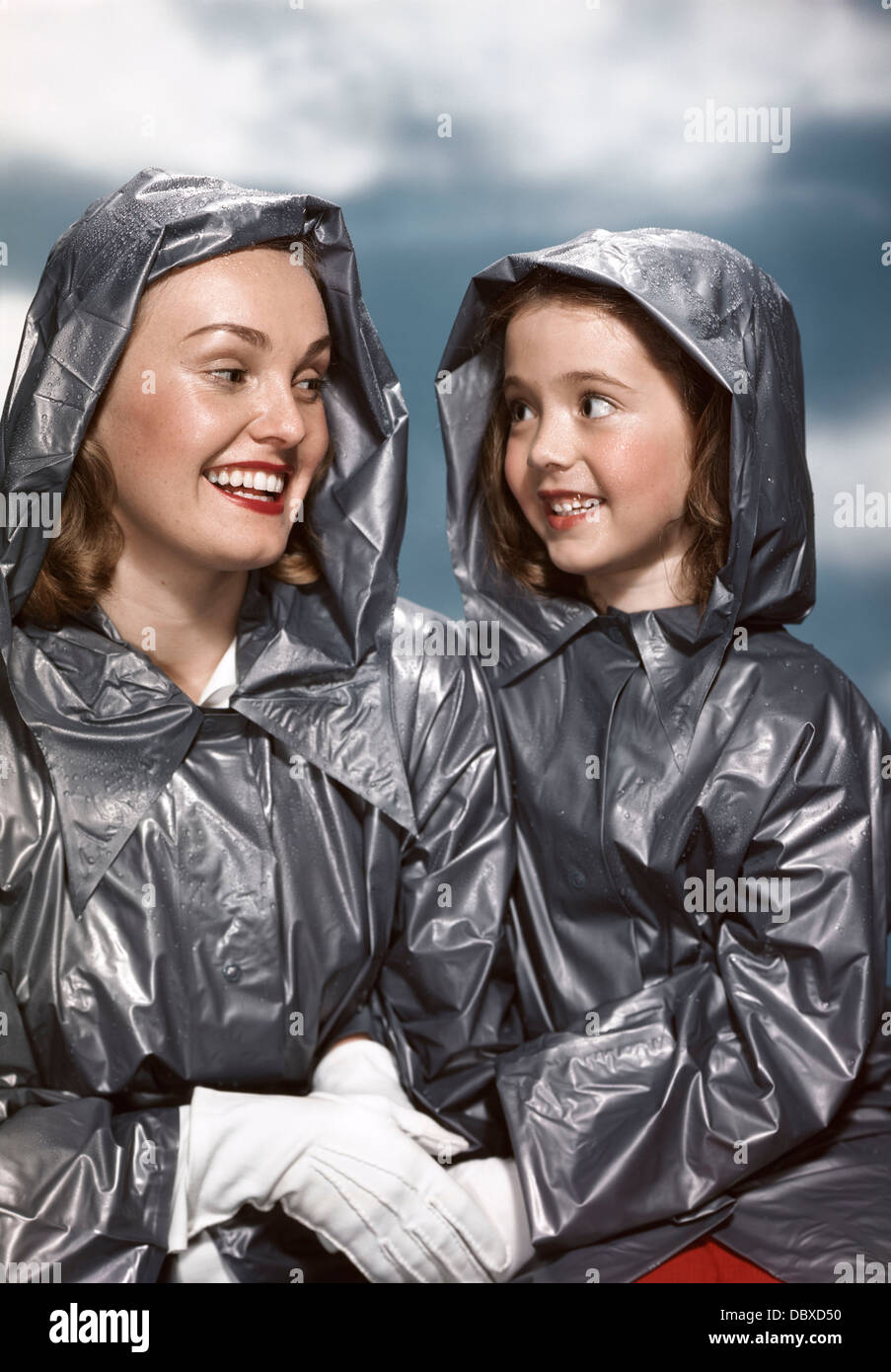 1940s 1950s PORTRAIT SMILING MOTHER AND DAUGHTER WEARING MATCHING RAIN COATS HOLDING HANDS Stock Photo