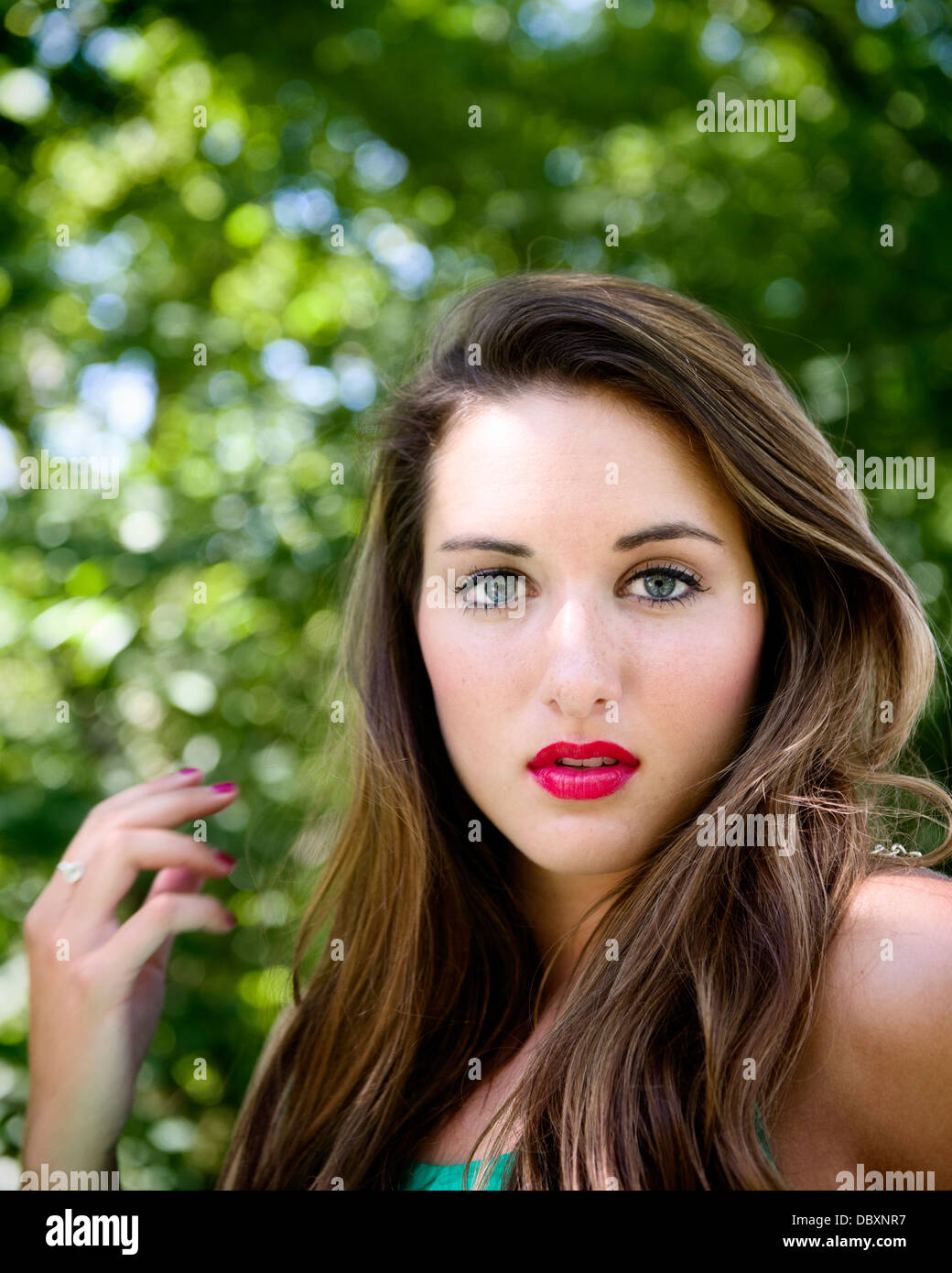 Portrait of attractive woman with brown hair outside with green leaves in the background Stock Photo