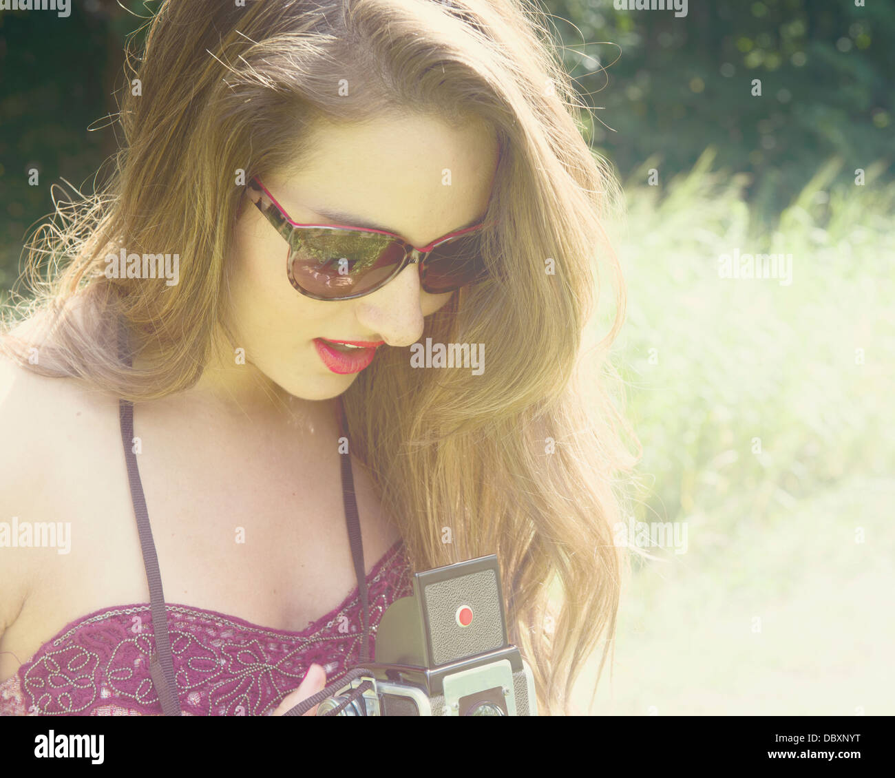 Young woman wearing sunglasses taking a photograph with a vintage camera. Stock Photo
